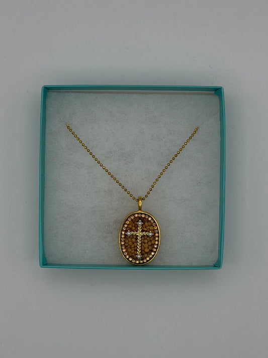 A gold cross pendant necklace displayed inside a square turquoise jewelry box with a white insert, set against a plain light gray background.